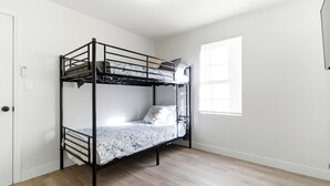 Ein Etagenbett in einem Zimmer mit Holzdielenboden, weißen Wänden und einem Fenster mit Jalousien.