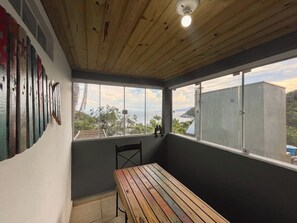 A balcony with a wooden table, a chair, and a view of the sea and hills. - At the top of Tainha beach, with a beautiful view that you can only find at Cabana do Abib. (Bombinhas)