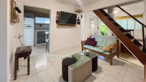 A spacious living area with a sofa, coffee table, and a TV mounted on the wall. A staircase leads to another level. - At the top of Tainha beach, with a beautiful view that you can only find at Cabana do Abib. (Bombinhas)