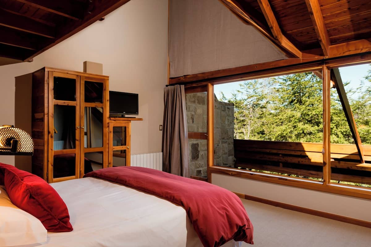 Quarto com cama grande, armário de madeira, televisão e janela com vista para árvores.