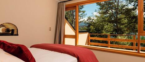 A bedroom with a large window, a bed with red and white bedding, and a wooden headboard.