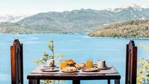 Una mesa con alimentos para el desayuno y una vista panorámica de un lago y montañas.