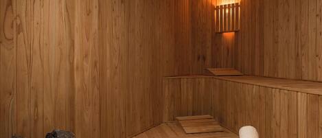 Un sauna en bois avec des bancs, une lampe fixée au mur et un tas de pierres.