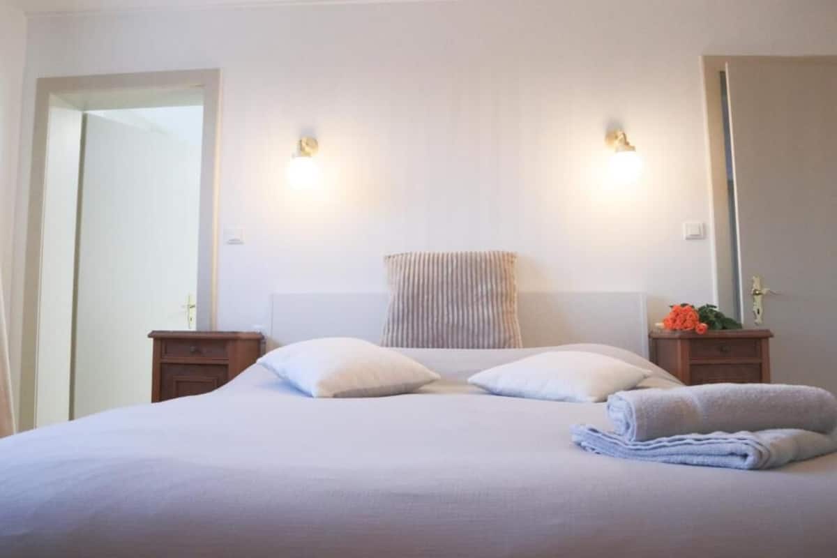Ett hotellrum med en säng, två sängbord, ett litet bord, en spegel och en väggmonterad lampa.
