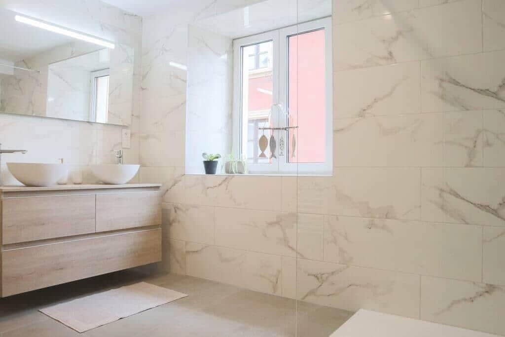 Une salle de bain avec un mur en marbre, une fenêtre, un lavabo et un miroir.