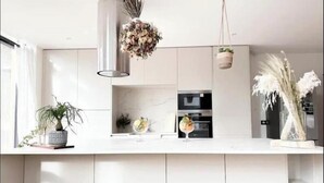 Une cuisine moderne avec des meubles blancs, un luminaire suspendu et des plantes décoratives.