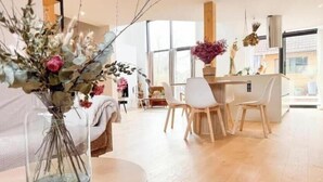 Un salon moderne avec un coin repas, de grandes fenêtres et un vase rempli de fleurs posé sur une table.