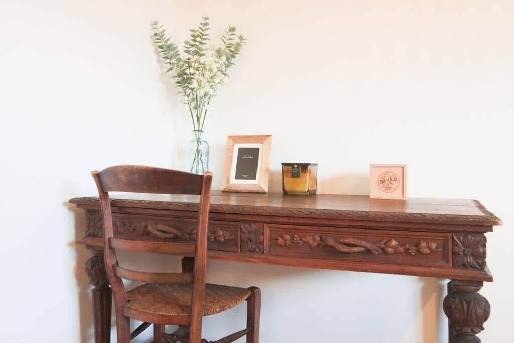 A wooden desk with a chair, a vase with flowers, and a framed picture.