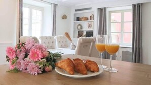 Une table à manger avec des croissants, du jus d’orange et des fleurs roses.