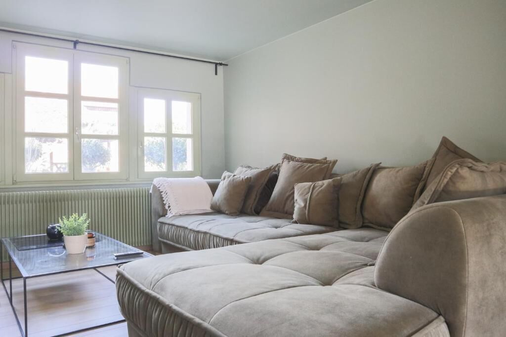 A living room with a sofa, a glass coffee table, and a window with blinds.