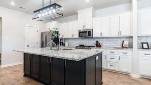 A modern kitchen with white cabinets, a black island, stainless steel appliances, and a geometric pendant light. - The Carlisle - 3BR/2BA - Family Friendly New Build (Lubbock)