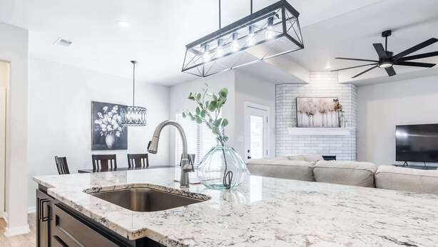 A modern kitchen with a granite countertop, stainless steel sink, and a dining area with chairs. - The Carlisle - 3BR/2BA - Family Friendly New Build (Lubbock)
