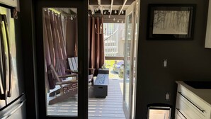 Eine offene Tür, die auf einen Balkon mit Blick auf einen Garten, eine Holzterrasse und einen Essbereich führt.