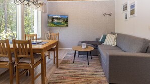 A cozy room with a wooden ceiling, a dining table with chairs, a gray sofa, a small coffee table, and a TV mounted on the wall. - Sevettijärventie 8753 by Interhome (Inari)