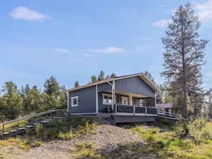 A modern house with a covered porch, a staircase leading up to it, and a forested backdrop.