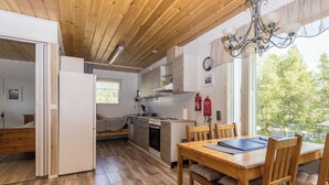 A compact kitchen with wooden cabinets, a dining area with a table and chairs, and a window with a view of greenery. - Sevettijärventie 8753 by Interhome (Inari)