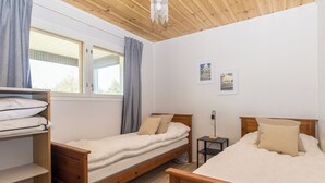 A bedroom with two wooden beds, a shelf with folded clothes, a bedside table with a lamp, and a window with curtains. - Sevettijärventie 8753 by Interhome (Inari)