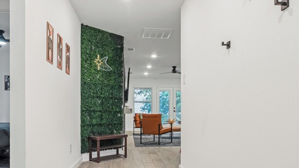 Un interior moderno con una pared verde, cuadros enmarcados y una zona de estar con una silla y un banco.