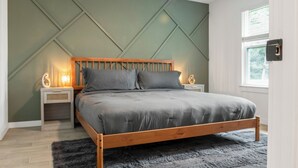 Un dormitorio con una cama de madera, dos mesitas de noche con lámparas, un ventanal grande y un diseño geométrico en la pared.