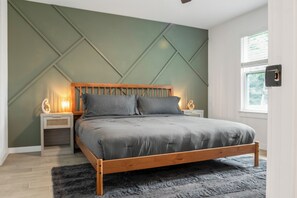 A bedroom with a wooden bed, two bedside tables with lamps, a large window, and a geometric wall design. - Hidden Lake Gem Arcade Stay (Denison)