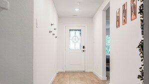 Un pasillo con una puerta blanca, suelo de madera clara y interruptores de luz en la pared.