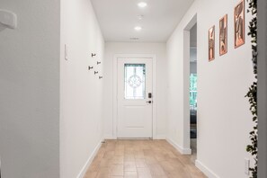 A hallway with a white door, light wood flooring, and wall-mounted light switches. - Hidden Lake Gem Arcade Stay (Denison)