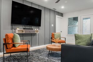 A modern living room with a flat-screen TV mounted on the wall, two leather chairs with cushions, a wooden coffee table, and a patterned rug. - Hidden Lake Gem Arcade Stay (Denison)