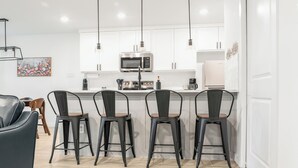 Una cocina moderna con gabinetes blancos, un microondas de acero inoxidable y una barra con cuatro taburetes.