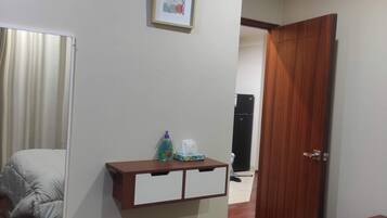 A bedroom with a bed, a bedside table with a mirror, a framed picture on the wall, and a door leading to another room.