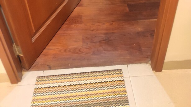 Een houten deur die leidt naar een eetruimte met een tafel en stoelen, een vloerkleed met dessin en een raam met gordijnen.