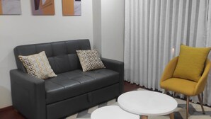 Een moderne woonkamer met een zwarte leren bank, twee witte ronde tafels, een gele fauteuil en abstracte wanddecoratie.