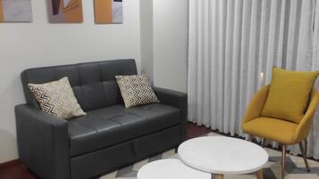A modern living room with a black leather sofa, two white round tables, a yellow armchair, and abstract wall art.