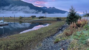 Una vista serena sobre un lago, con montañas al fondo, un muelle y un pequeño edificio.
