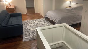 Un dormitorio con cama, sofá azul, alfombra estampada, mesita de noche y lámpara.