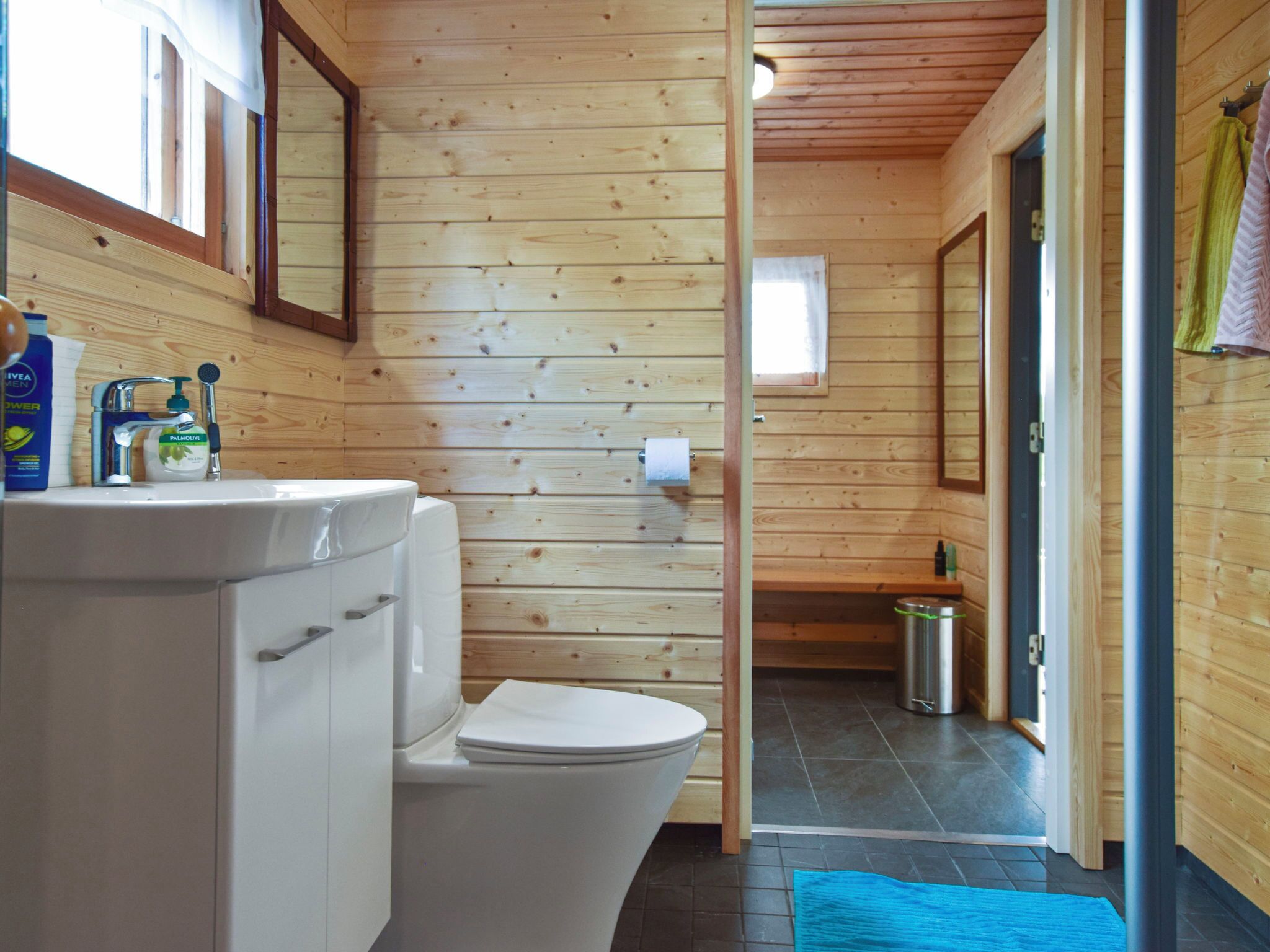 A wooden cabin interior with a bathroom, including a sink, toilet, and a small window.
