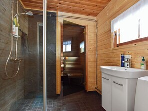 Ein Badezimmer mit Dusche, Toilette und Waschbecken, Holzwänden und einer Bank im Hintergrund.