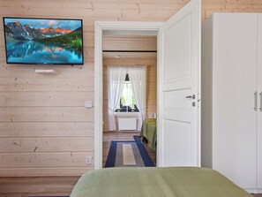 Una habitación con cama, televisión en la pared, escritorio con silla y armario.