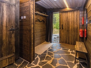A rustic wooden room with a stone floor, a bench, and a door leading outside.