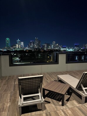 A rooftop terrace with two lounge chairs and a table, overlooking a city skyline at night. - Luxury Modern Downtown Dallas / Farmers Market (Dallas)