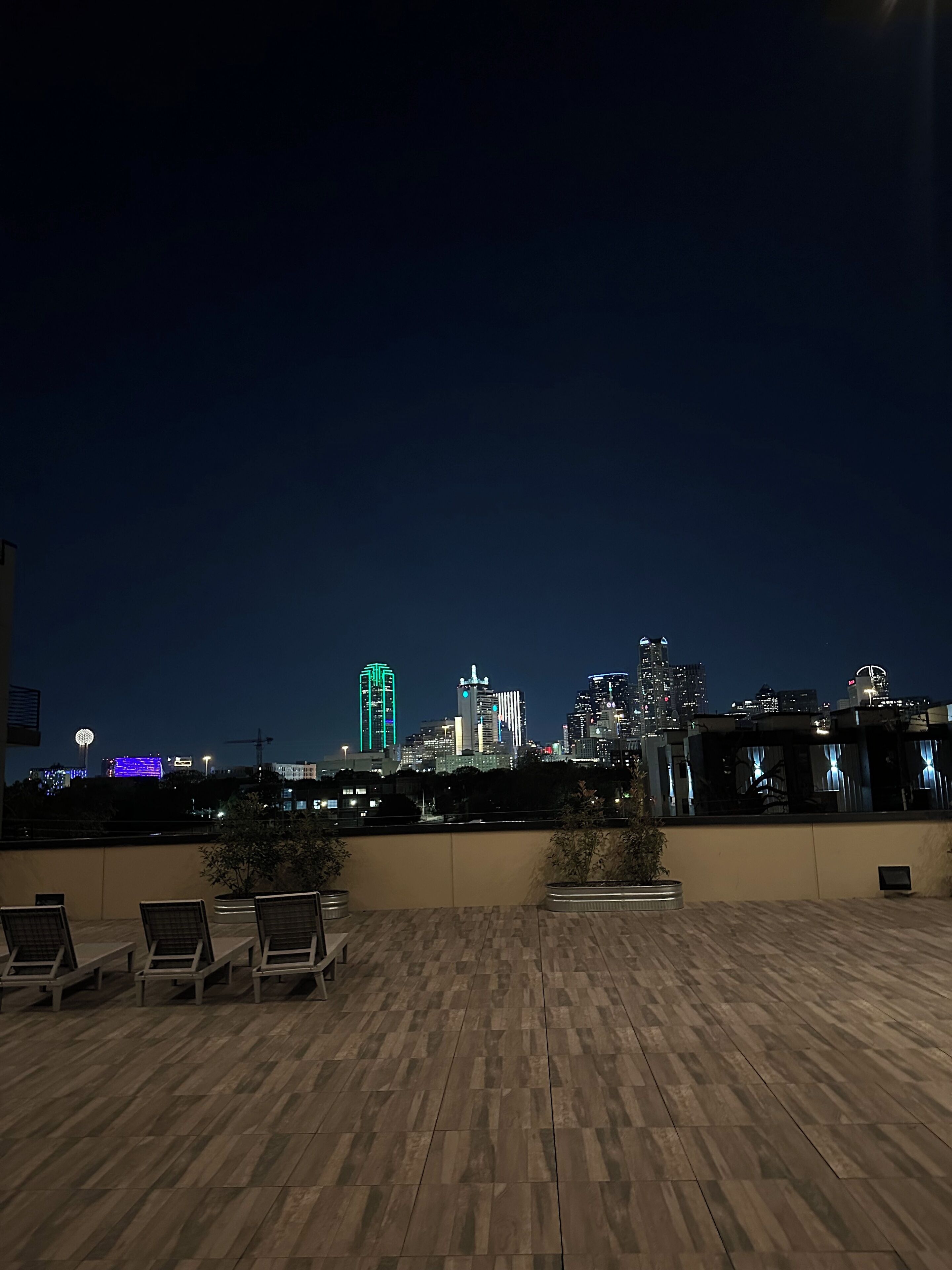 A rooftop terrace with lounge chairs and a city skyline in the background.