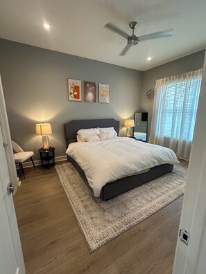 Un dormitorio con cama, lámparas de noche, ventilador de techo y una obra de arte en la pared.