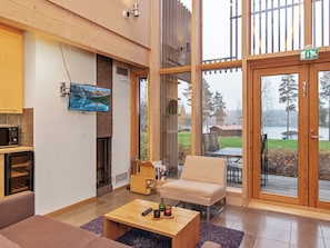 A modern living room with a fireplace, a television mounted on the wall, a sofa, a coffee table, and a view of a lake through large glass doors.