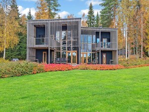 A modern two-story house with a wooden exterior, large windows, and a well-maintained lawn.