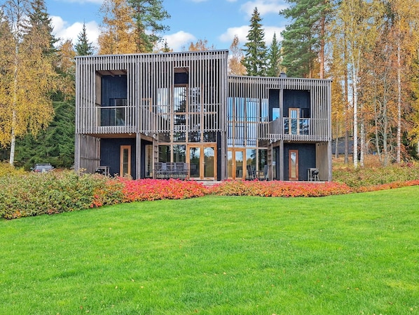 A modern two-story house with a wooden exterior, large windows, and a well-maintained lawn.