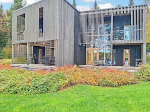 A modern two-story building with a wooden exterior, large windows, and a deck area.