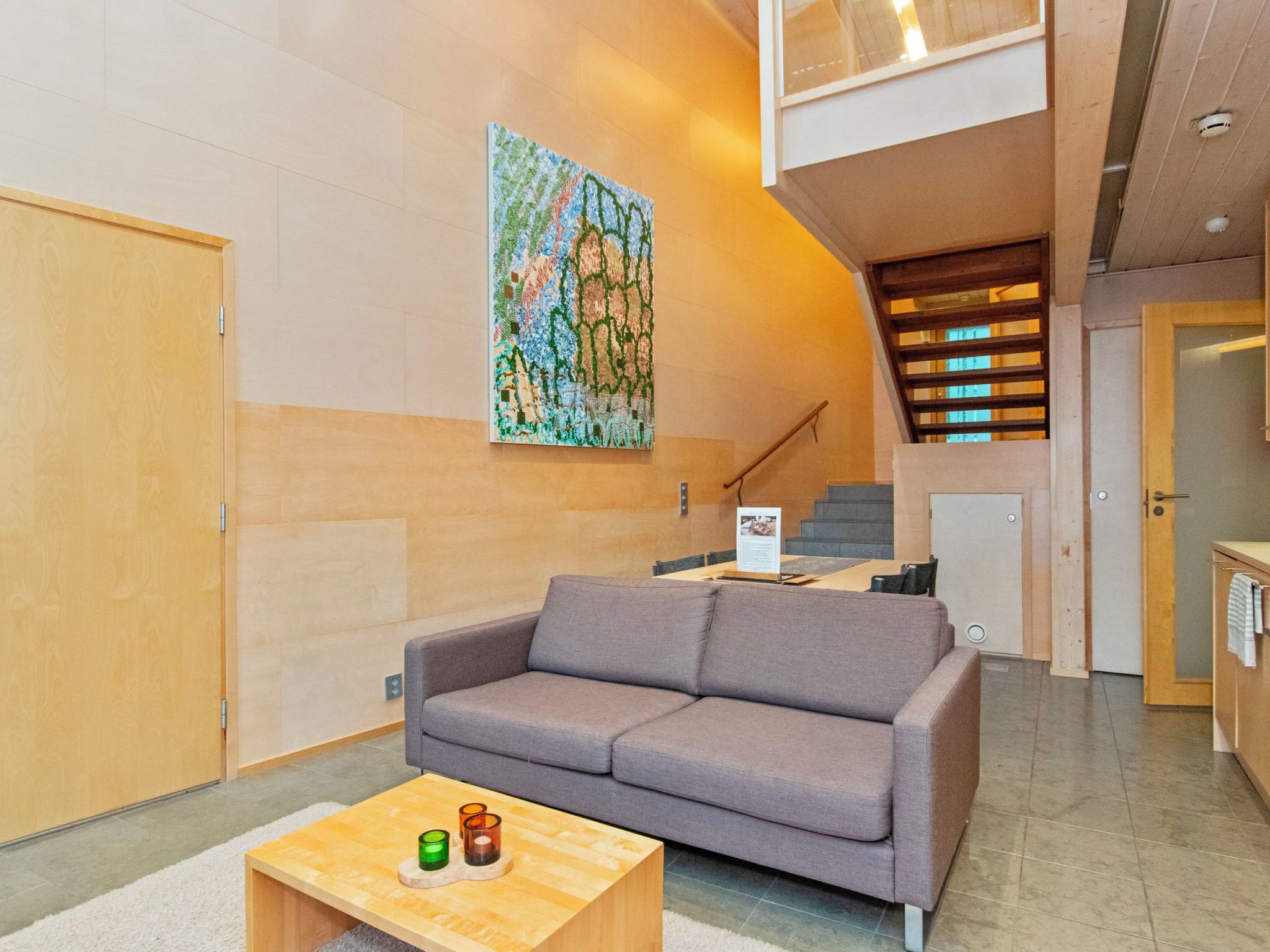 Ein modernes Interieur mit einem grauen Sofa, einem Holztisch und einem farbenfrohen abstrakten Gemälde an der Wand.