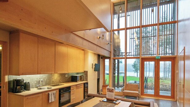 A modern kitchen with wooden cabinets, a dining area with a table and chairs, and large windows offering a view of the outdoors. - Villa sinikka 1 by Interhome (Mikkeli)