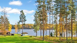A lakeside property with a grassy lawn, a small cabin, and tall trees. - Villa sinikka 1 by Interhome (Mikkeli)