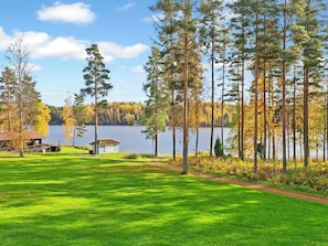A lakeside property with a grassy lawn, a small cabin, and tall trees.