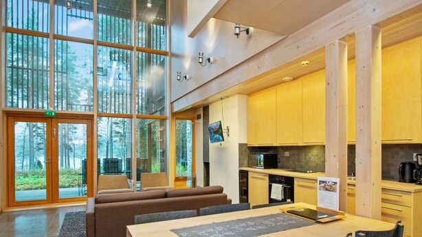 A modern interior with a dining area, kitchen, and large glass doors leading to a forest view. - Villa sinikka 2 by Interhome (Mikkeli)